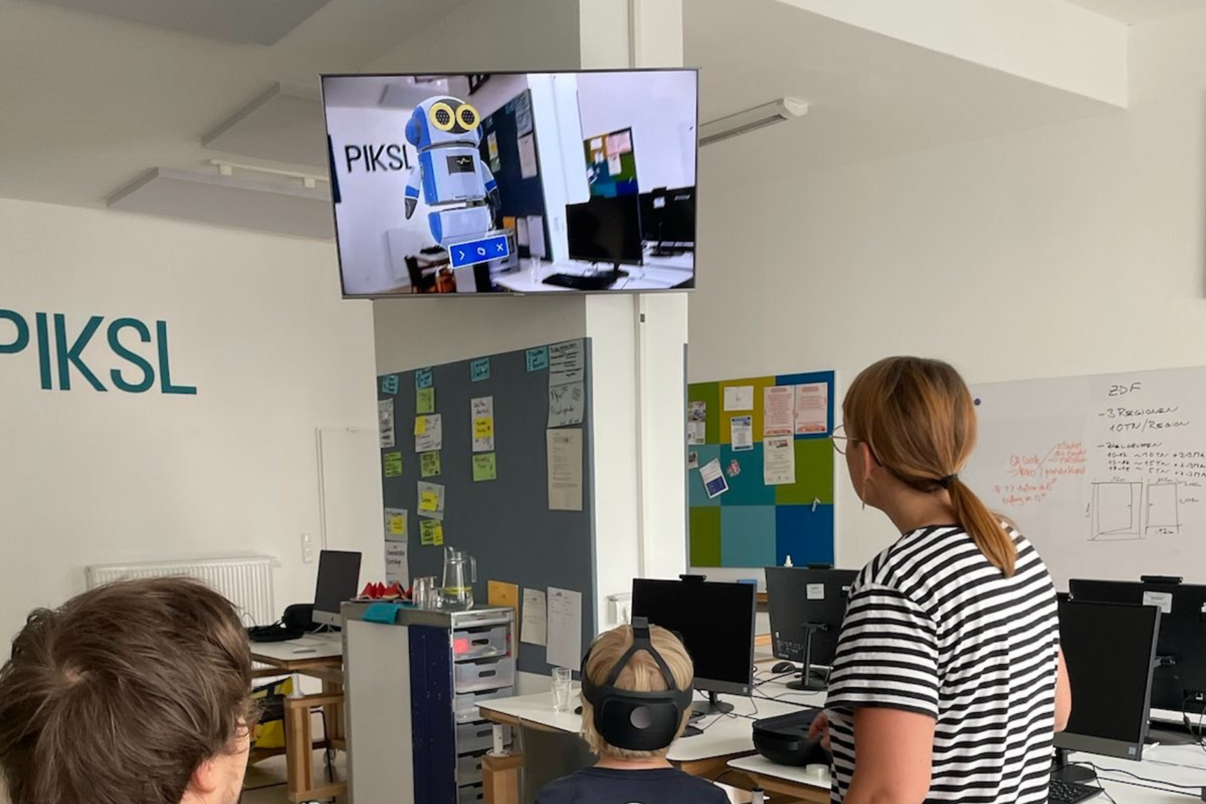 Ein Kind mit Virtual-Reality-Brille steuert einen virtuellen Roboter, der auf einem Bildschirm zu sehen ist