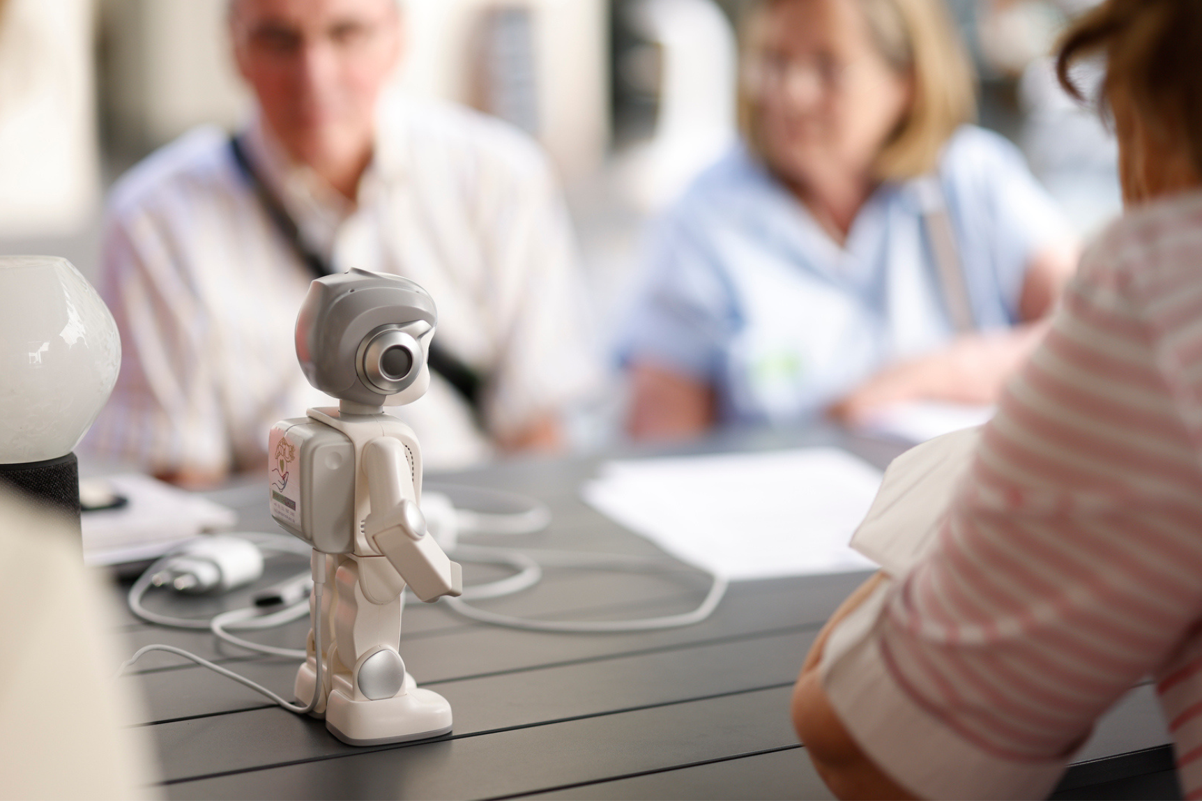 Ältere Menschen schauen sich einen kleinen Roboter an, der auf dem Tisch steht