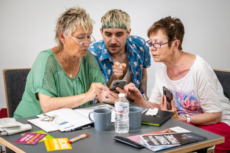 Ein jüngerer Mann erklärt zwei älteren Frauen etwas am Smartphone.